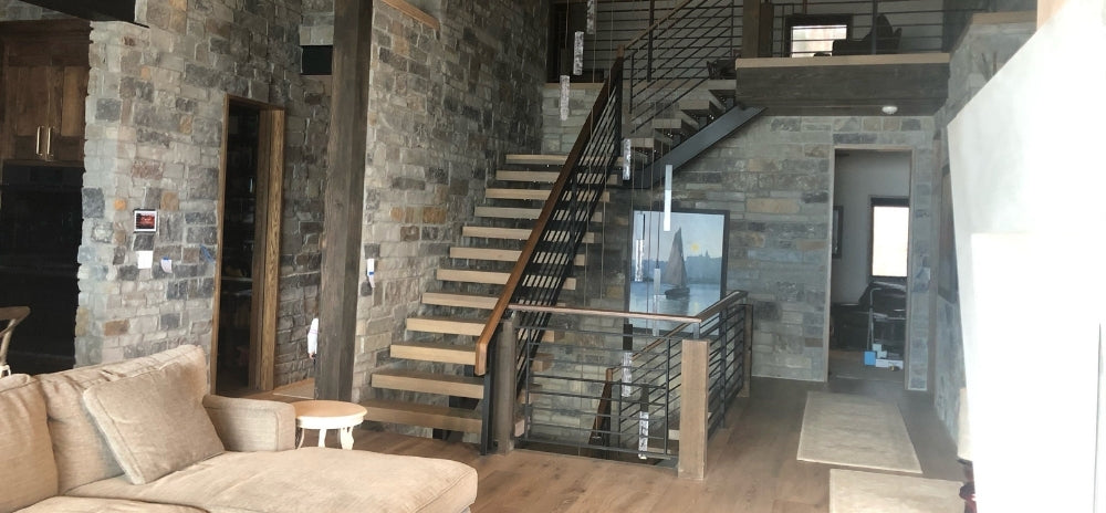 Modern living space with stone walls and a staircase, featuring a flush-mounted ELAN 8" touch panel on the wall.