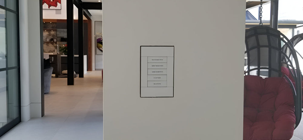 Crestron keypad recessed into a SeeLess flush wall mount, installed in a modern open-space interior with neutral tones and contemporary furnishings.